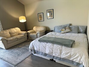 Ein Schlafzimmer mit einem Bett, zwei Stühlen, einem Teppich und einer Lampe.