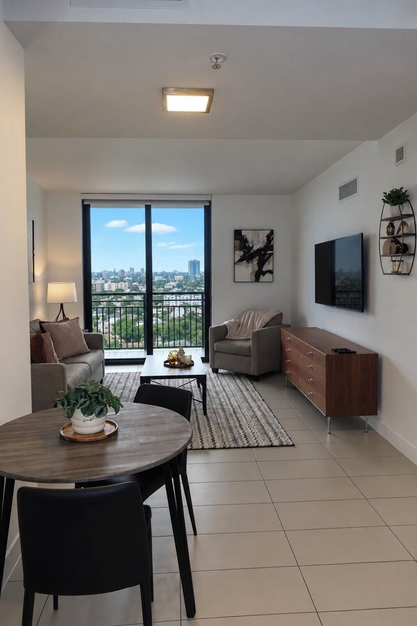 A modern living room with a dining area, a sofa, a TV, and a large window with a city view.