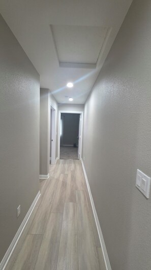 A hallway with a light-colored floor, white walls, and a ceiling with recessed lighting.