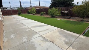 A backyard with a concrete patio, a well-maintained lawn, a wooden fence, and a small table.
