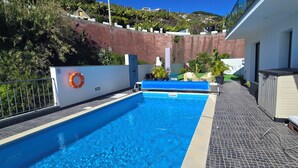 Ein Schwimmbecken mit Rettungsboje, eine Lounge mit einer Couch und Blick auf einen Hügelhang.