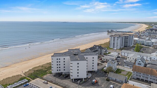 Un hotel costero con varias edificaciones, un estacionamiento y una playa al fondo.