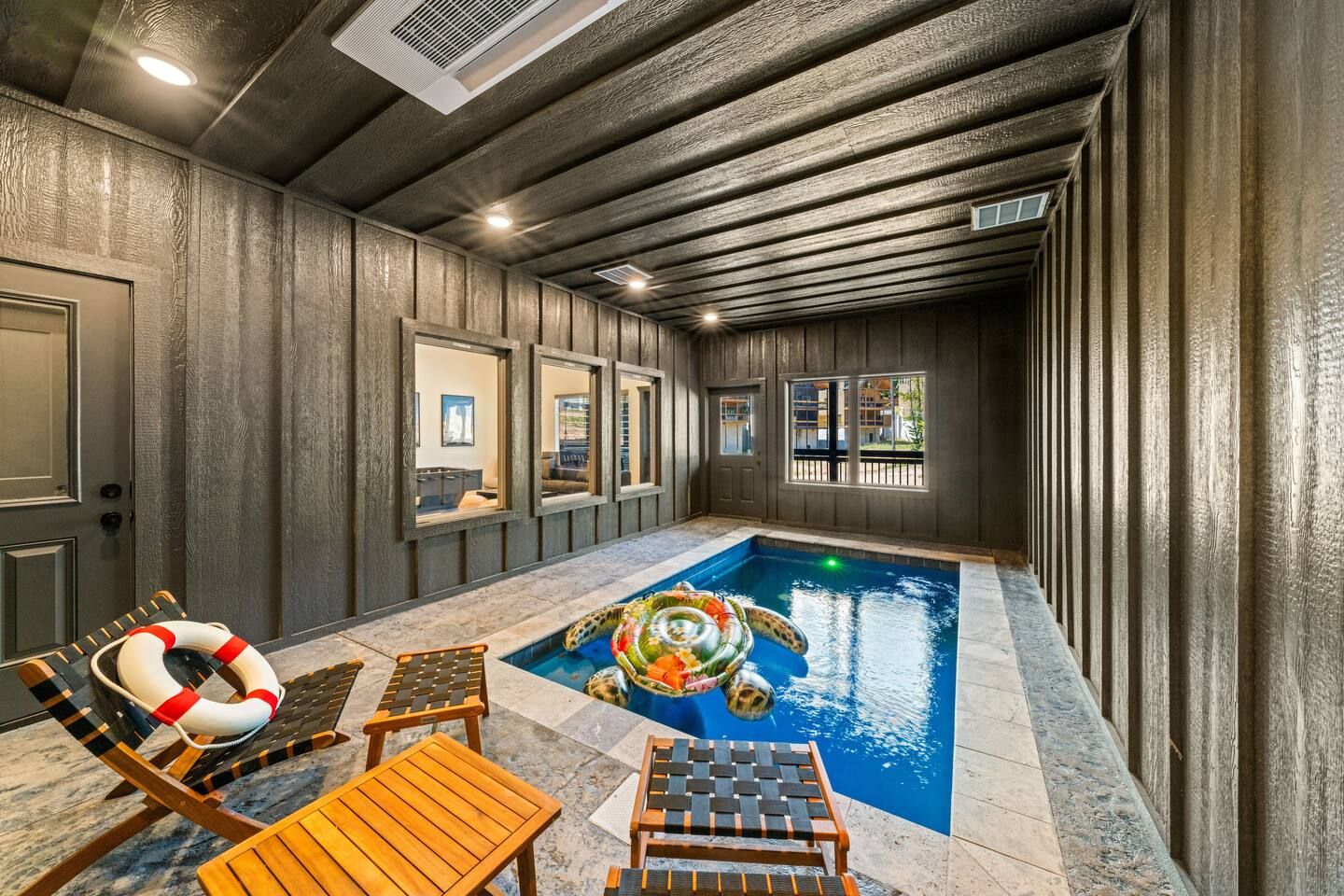 An indoor swimming pool with lounge chairs and a lifebuoy, surrounded by wooden walls and windows.