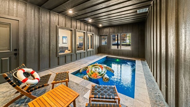 Una piscina interna con lettini da relax e un galleggiante, circondata da pareti e finestre in legno.