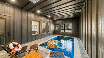 An indoor swimming pool with lounge chairs and a lifebuoy, surrounded by wooden walls and windows.