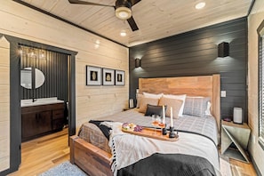 A modern bedroom with a wooden headboard, a bedside table with a tray of snacks, and a mirror above the vanity. - LUXE-Pool-Pets-1 Mi to PKWY-Hot Tub-Games (Pigeon Forge)
