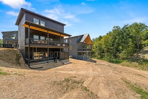 A modern two-story house with a balcony, a covered porch, and a dirt driveway. - LUXE-Pool-Pets-1 Mi to PKWY-Hot Tub-Games (Pigeon Forge)