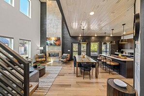 A spacious living area with a fireplace, dining table, and seating, featuring a modern kitchen and a staircase. - LUXE-Pool-Pets-1 Mi to PKWY-Hot Tub-Games (Pigeon Forge)