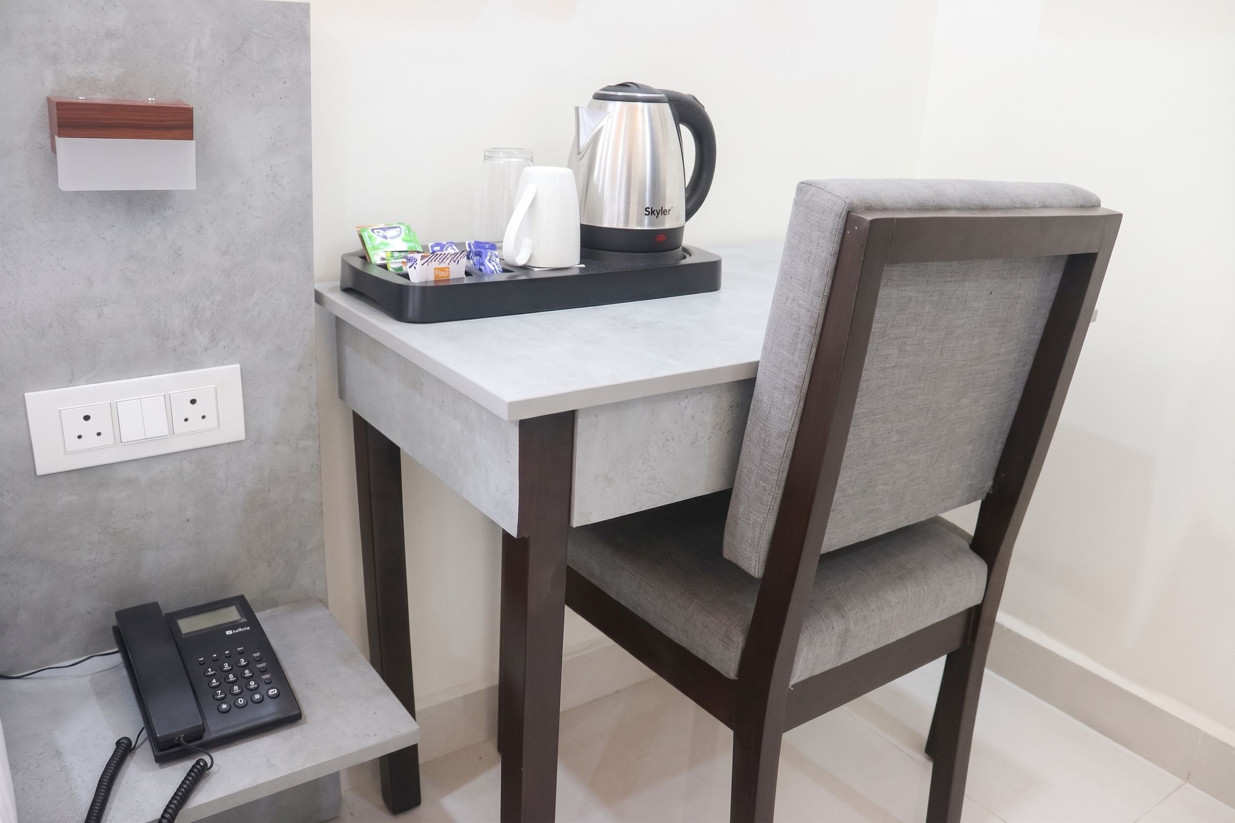 Una kitchenette pequeña y moderna con cafetera, hervidor de agua y una bandeja con alimentos envasados.