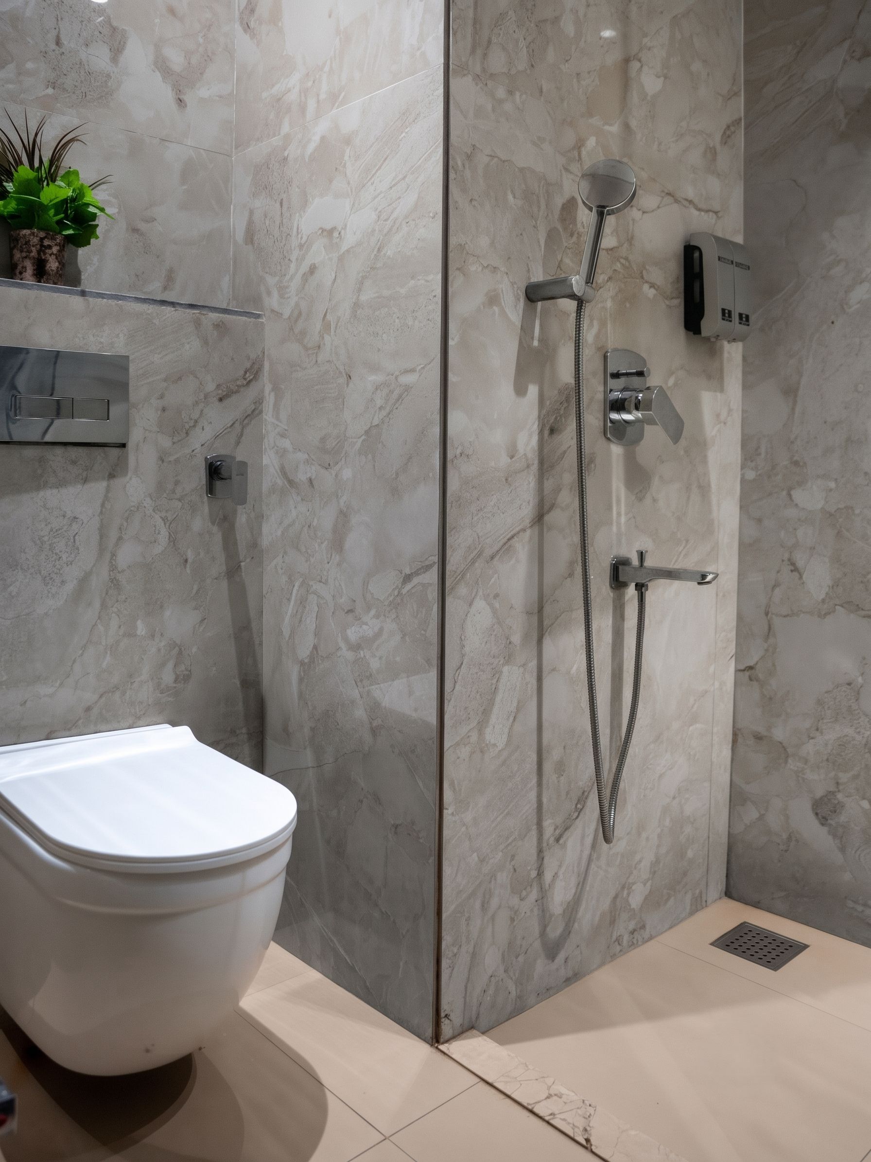 Une salle de bain moderne équipée de toilettes, d’une douche avec un pommeau de douche à main et d’un distributeur de savon fixé au mur.
