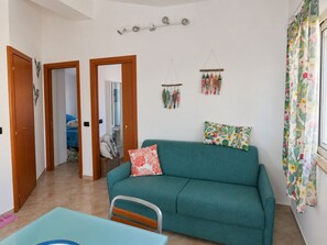 Quarto com um sofá azul-turquesa, uma mesinha e uma janela com cortinas florais.