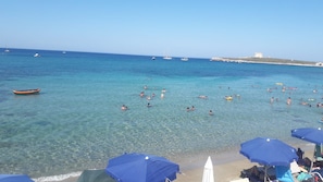 Ein Strand mit klarem türkisblauem Wasser, Menschen beim Schwimmen und Booten in der Ferne.