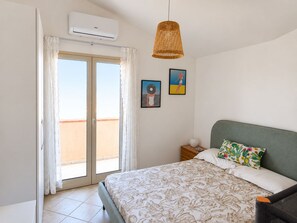 A bedroom with a bed, a nightstand, a wicker pendant light, and a sliding glass door leading to a balcony. - The sea and the sun: The beach is within walking distance, and the house is comfortable and bright—everything is within easy reach. (Unknown)