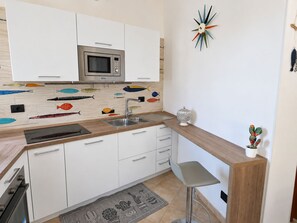 A kitchen with white cabinets, a stainless steel microwave, a sink, and a bar stool. - Sea and sun: the beach is within walking distance, and the house is comfortable and bright—everything is right at your fingertips. (Unknown)