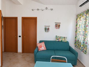A room with a teal sofa, a small table, and a wall-mounted light fixture. - Sea and sun: the beach is within walking distance, and the house is comfortable and bright—everything is right at your fingertips. (Unknown)