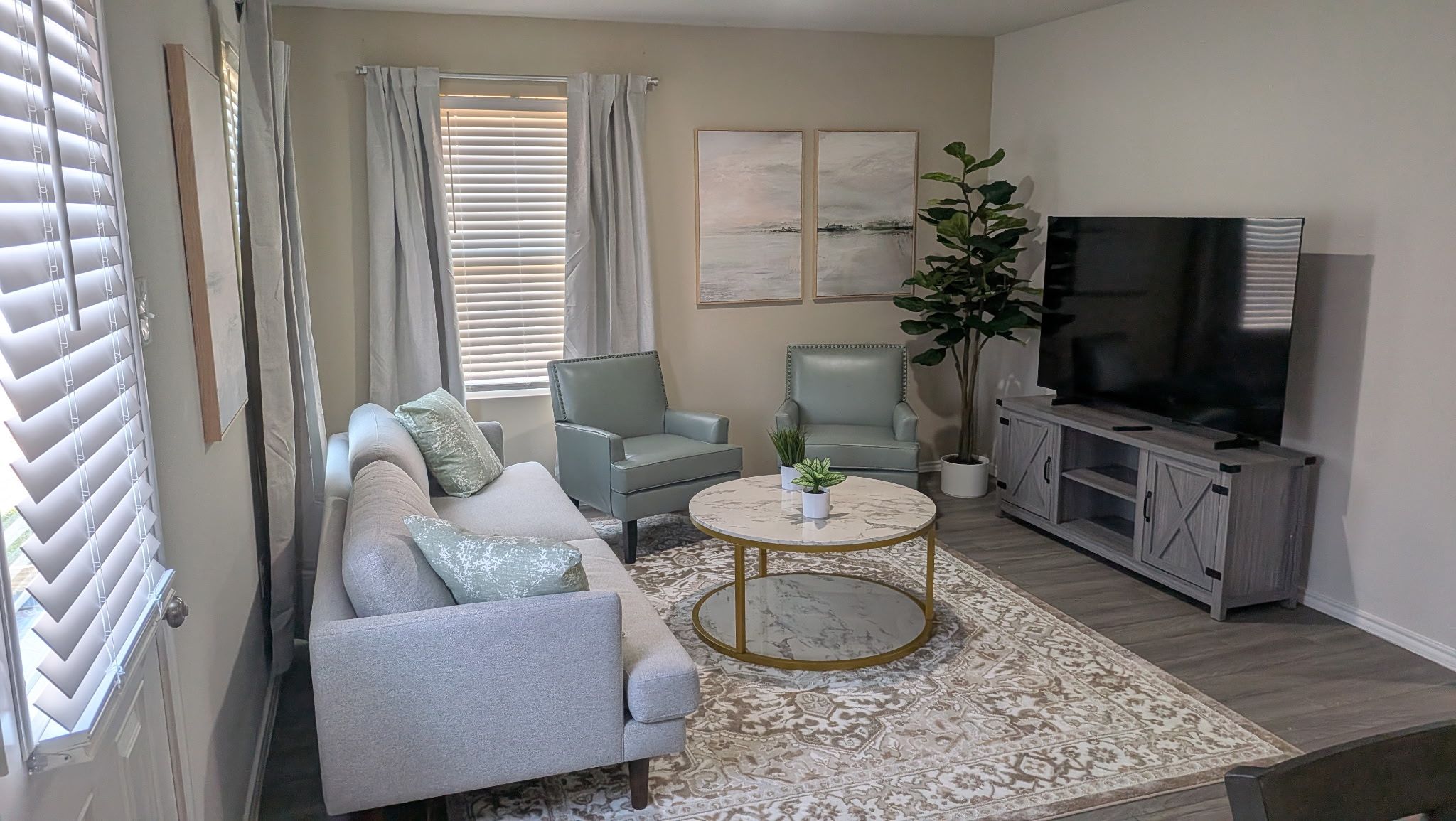A living room with a sofa, armchairs, a coffee table, a TV, and a potted plant.