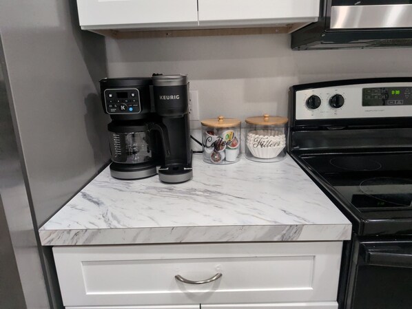 A kitchen with a coffee maker, two containers labeled 'Coffee' and 'Filters,' and a stove.