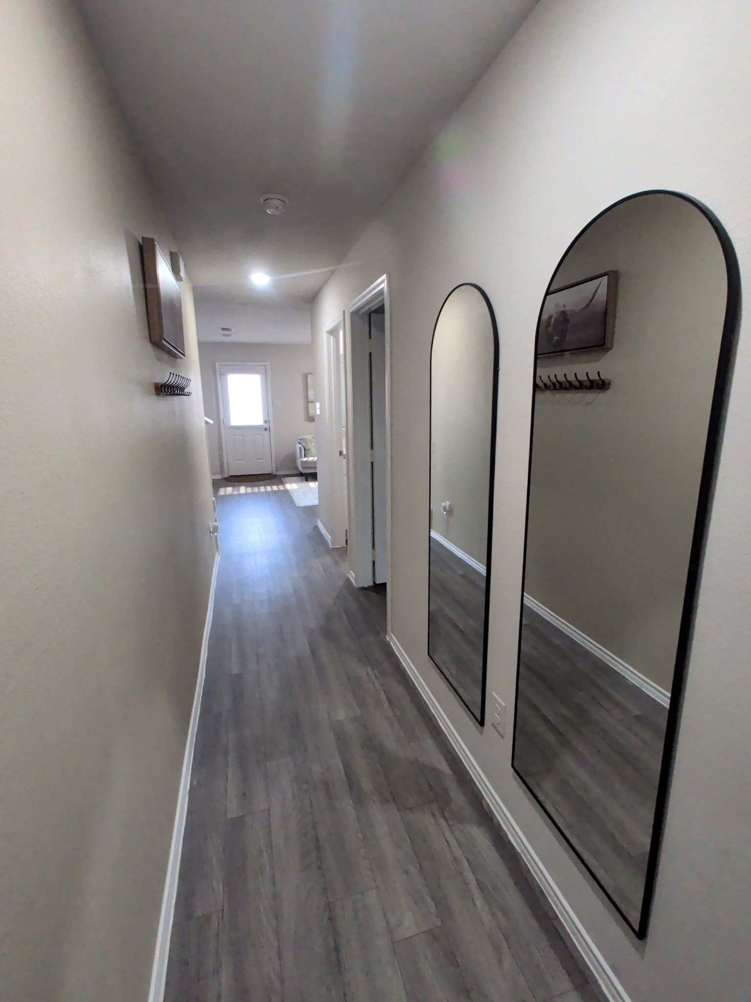 A hallway with a wooden floor, white walls, and a door at the end.