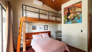 Una habitació amb un llit superposat, un llit amb un edredó rosa, terres de fusta, un quadre a la paret i una finestra amb cortines.