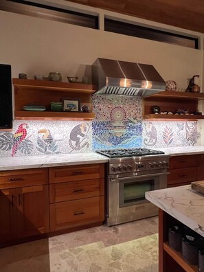 A kitchen with a gas stove, oven, wooden cabinets, and a decorative backsplash. - Casa Cavu - Luxury Jungle Home & Pool in Dominical (Platanillo)