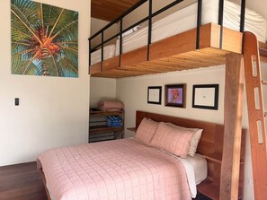 A bunk bed with a wooden frame and a single bed below. There is a shelf with folded clothes and a framed picture on the wall. - Casa Cavu - Luxury Jungle Home & Pool in Dominical (Platanillo)