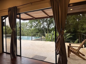 A room with large sliding glass doors leading to an outdoor area with a pool and greenery. - Casa Cavu - Luxury Jungle Home & Pool in Dominical (Platanillo)