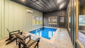 Une piscine intérieure dotée d’un sol carrelé, de chaises longues en bois et d’un plafond avec des spots encastrés.