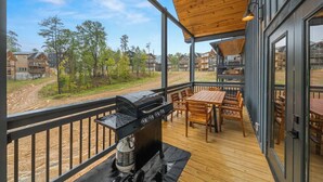 Un espace extérieur abrité, équipé d’un barbecue et de sièges, qui offre une vue sur un quartier résidentiel avec ses maisons et ses arbres.