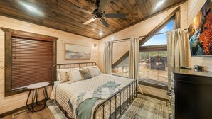 Une chambre avec un lit, une petite table, un ventilateur de plafond et une vue sur l’extérieur.