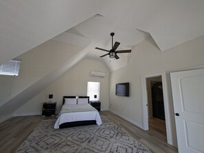 A bedroom with a sloped ceiling, a bed, a nightstand, a wall-mounted air conditioner, and a door. - Andy's Inn 4 Luxury Loft Apartment (Bodden Town)