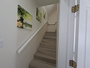 A staircase with a handrail, white walls, and three framed pictures on the wall. - Andy's Inn 4 Luxury Loft Apartment (Bodden Town)