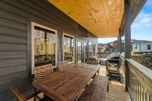 Eine Holzterrasse mit Tisch, Stühlen, einem Grill und Blick auf ein Haus im Hintergrund.