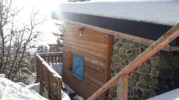 A wooden cabin with a stone wall, a wooden door, and a metal gate.