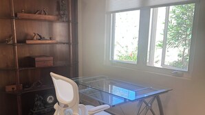 Een kamer met een glazen bureau, een witte bureaustoel, een houten boekenkast en een raam met jaloezieën.