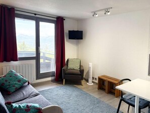 Ein Zimmer mit einer Couch, einem Sessel, einem kleinen Tisch, einem Standheizgerät und einem an der Wand befestigten Fernseher.