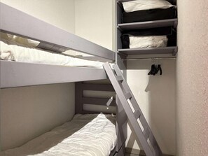 Ein Etagenbett mit einer Leiter, ein Regal mit gefalteter Kleidung und ein Haken zum Aufhängen.