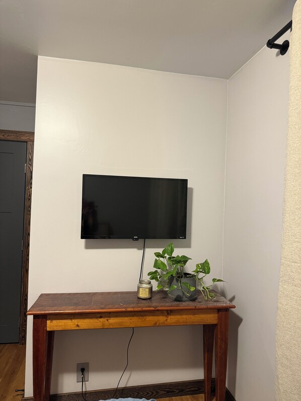 A room with a mounted flat-screen TV, a wooden table, and a potted plant.
