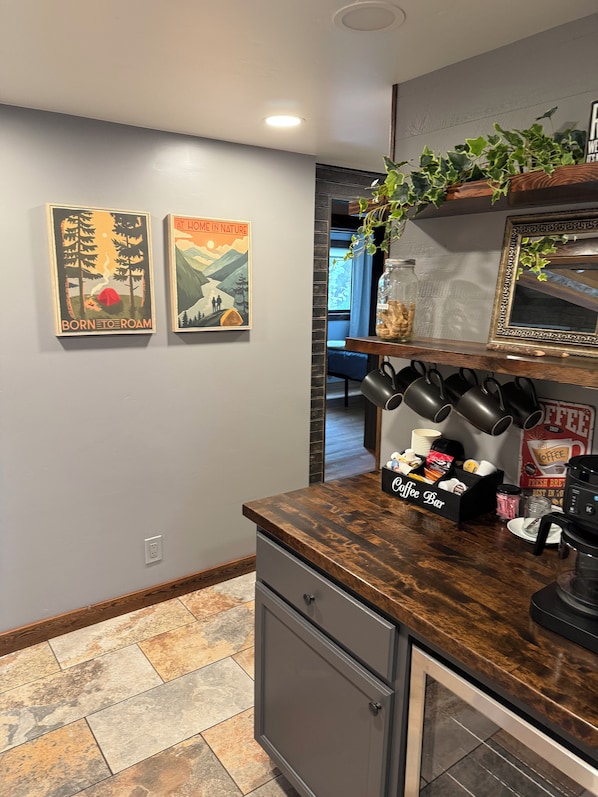 A kitchen with a coffee bar, two wall-mounted posters, and a plant on a shelf.