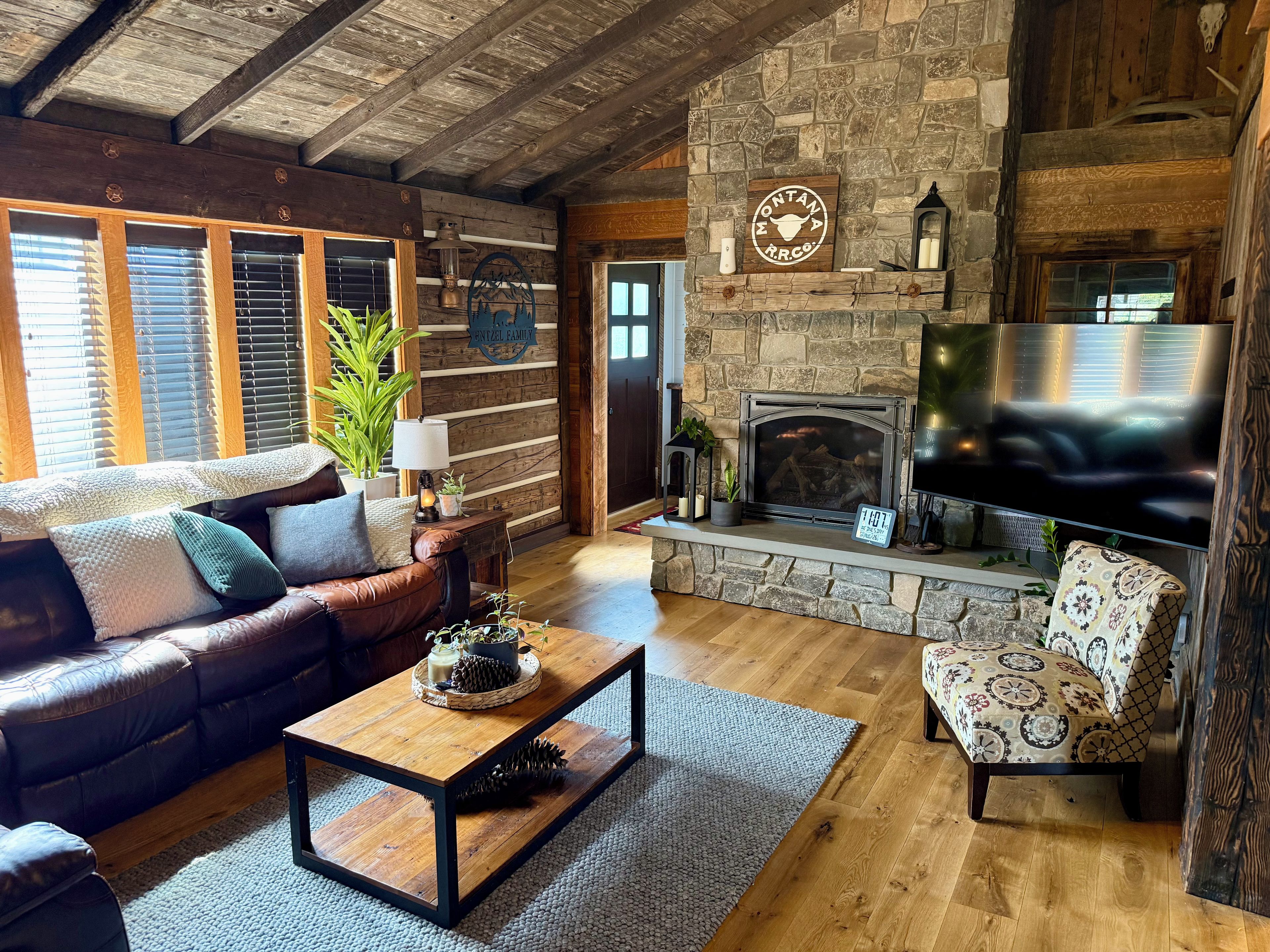 A cozy living room with a stone fireplace, leather sofa, and a flat-screen TV.