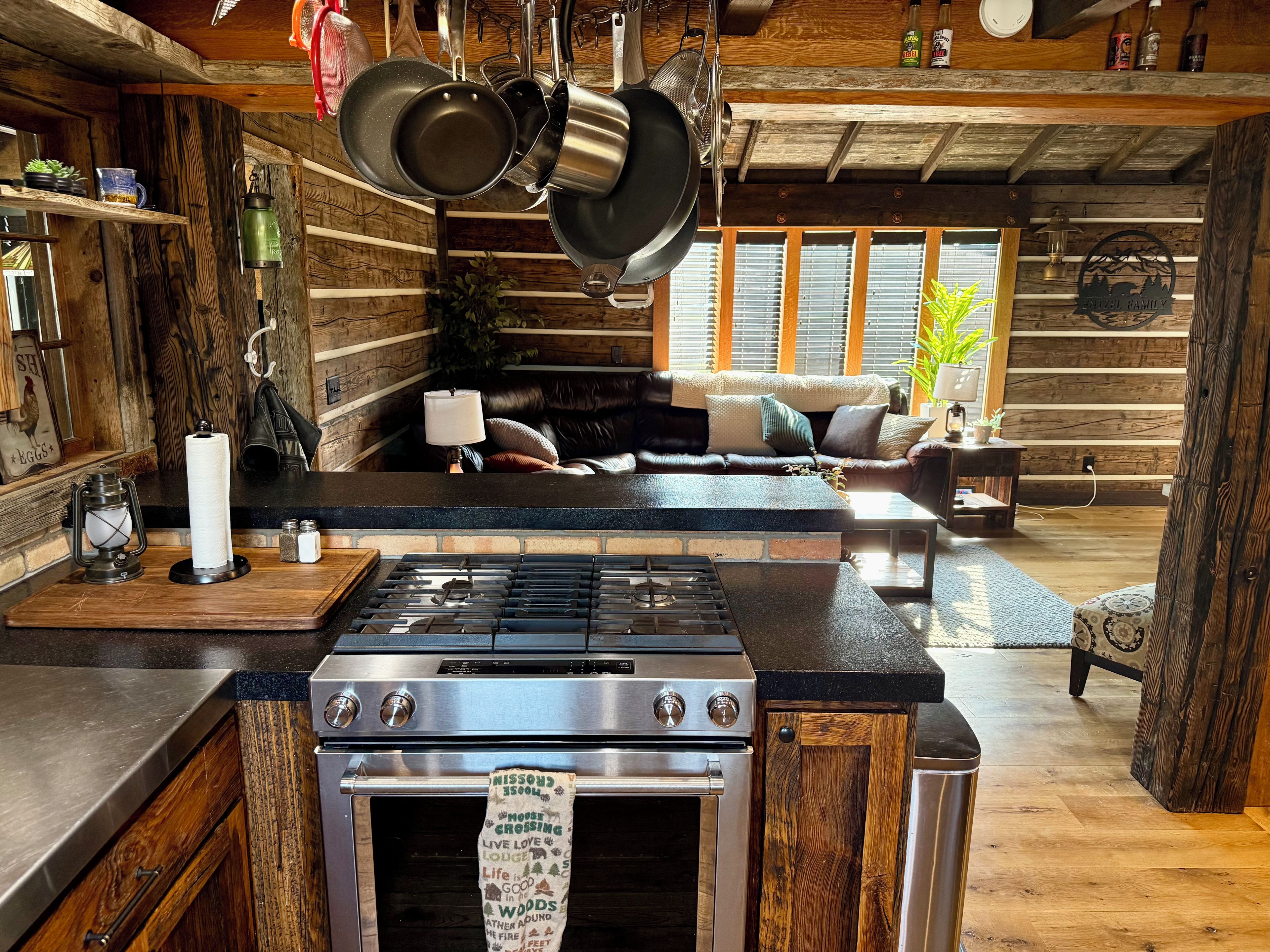 A rustic kitchen with a central island stove, wooden cabinetry, and hanging pots.