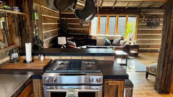 A rustic kitchen with a central island stove, wooden cabinetry, and hanging pots.
