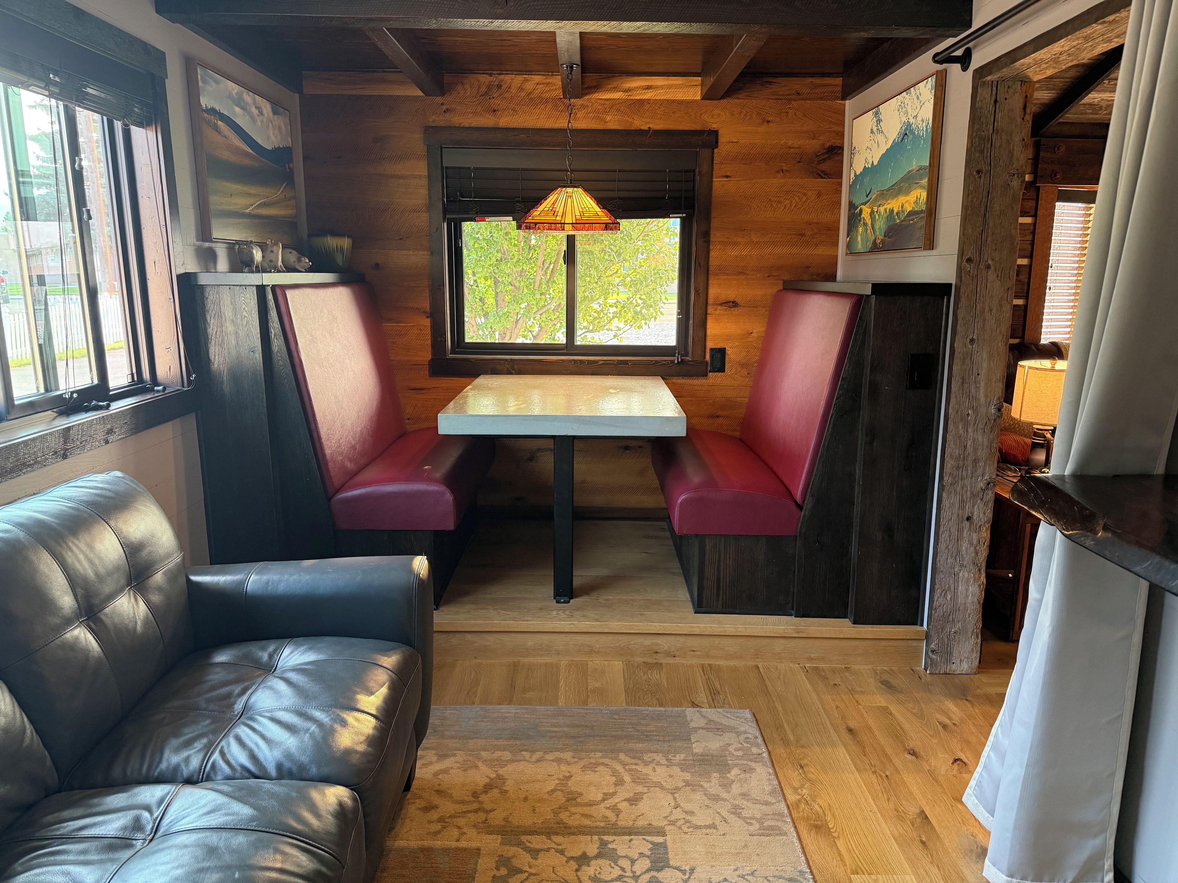 A cozy interior with a leather couch, wooden walls, a table with benches, and artwork.