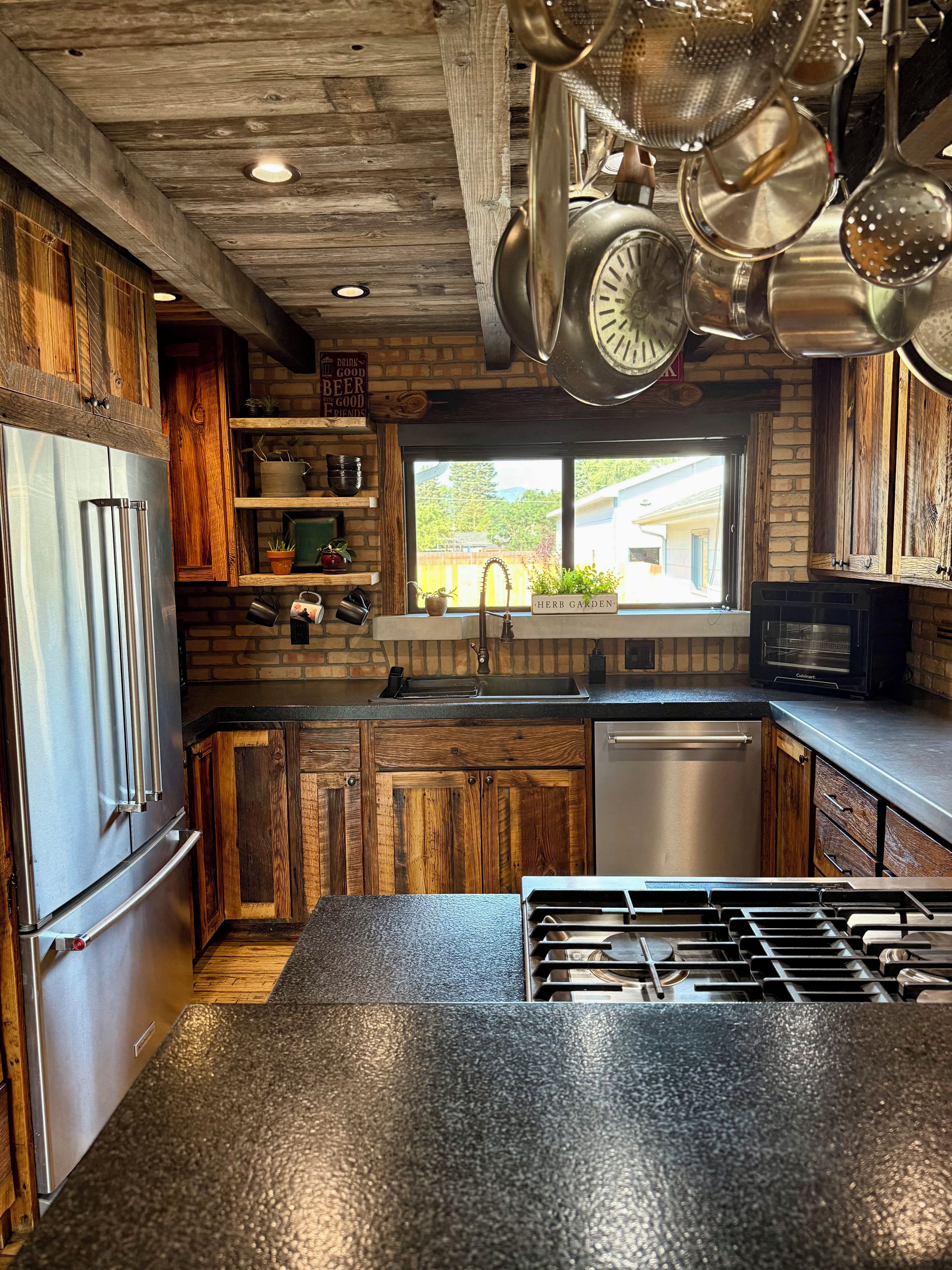 A kitchen with wooden cabinets, a stainless steel refrigerator, a gas stove, and hanging pots.