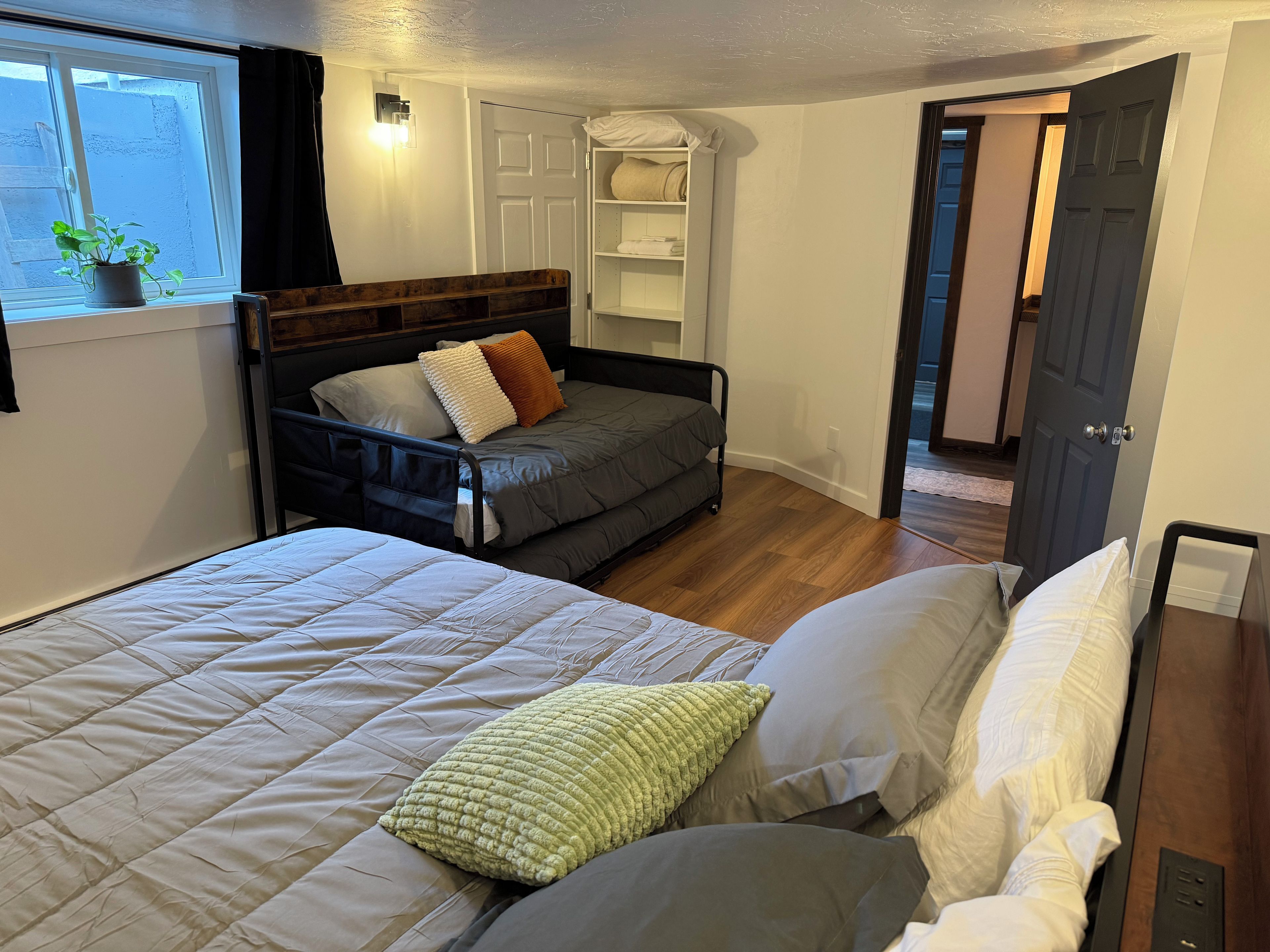 Een slaapkamer met een bed, een slaapbank, een nachtkastje, een kledingkast en een raam met een plant.