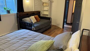 Een slaapkamer met een bed, een slaapbank, een nachtkastje, een kledingkast en een raam met een plant.