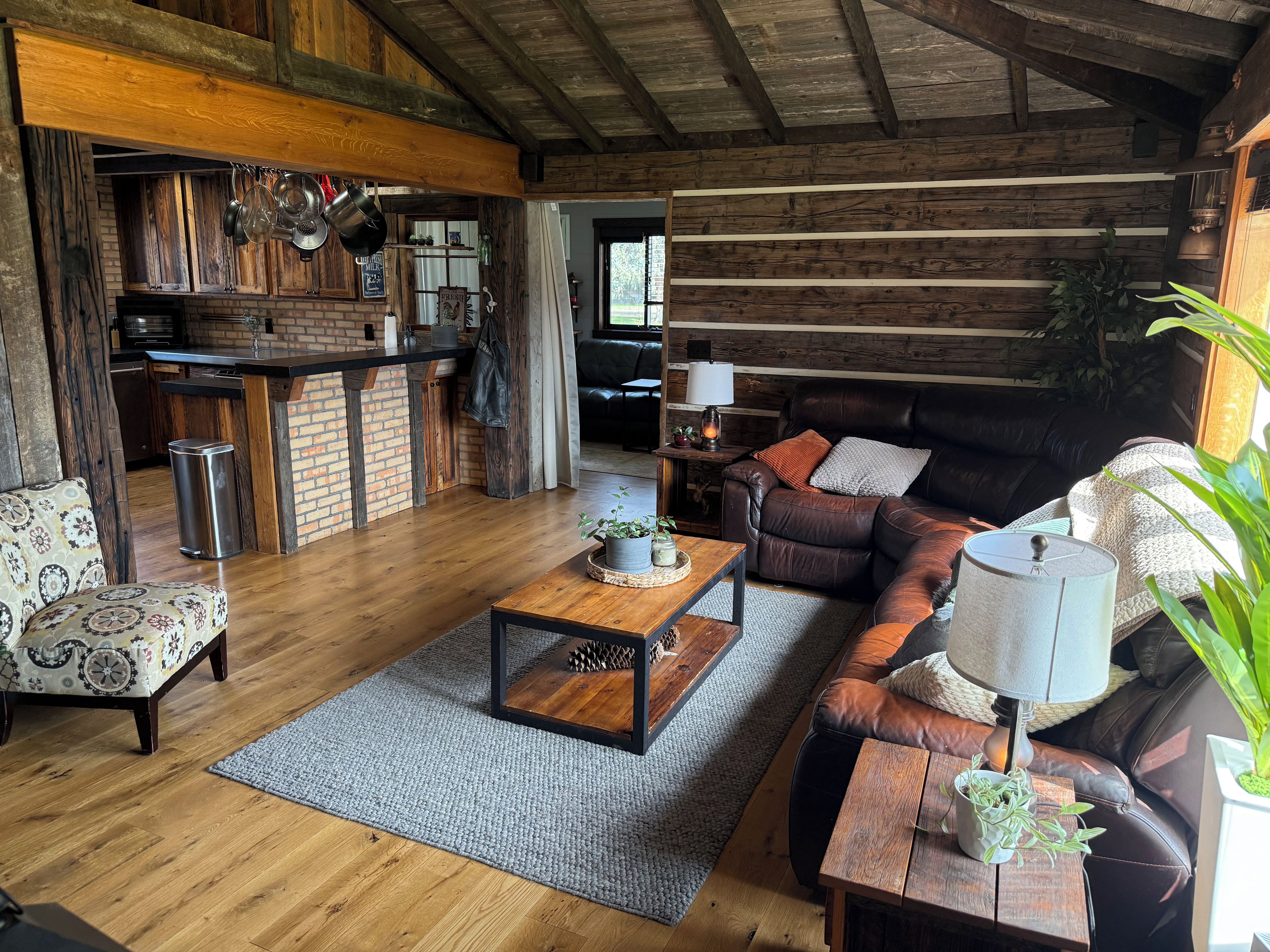 A rustic living room with a leather sofa, a wooden coffee table, and a kitchen area with hanging pots.