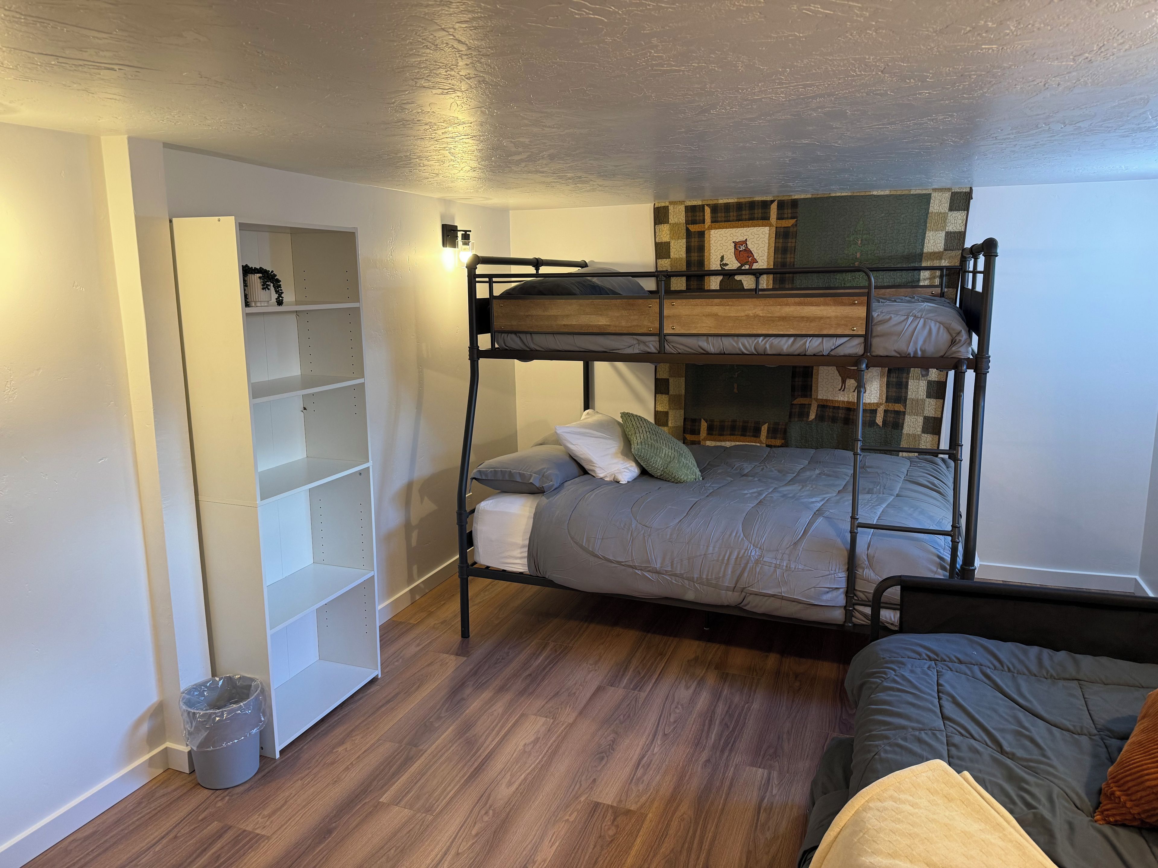 A bunk bed with a lower bunk, a bedside table, and a wall-mounted shelf unit.