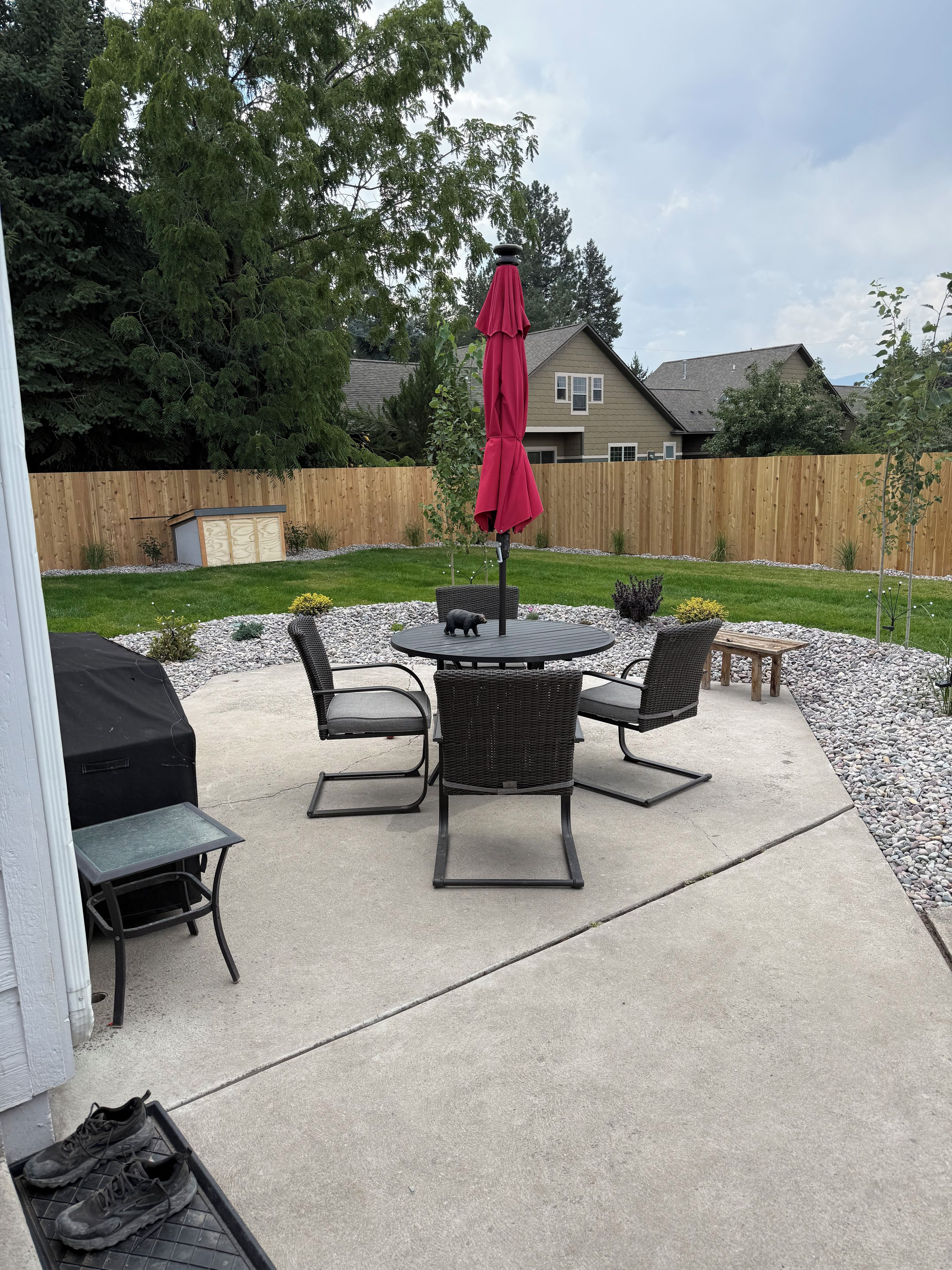 An outdoor patio with a round table, chairs, and a red umbrella.