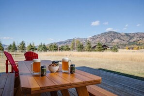 A wooden table with a beer mug, a can, and a bowl of snacks on a deck with a mountain view. - Foosball, Fireplace, Deck, Views, Guest Favorite (Alpine)