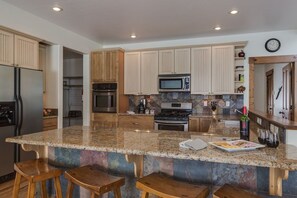 A kitchen with granite countertops, wooden cabinets, stainless steel appliances, and a bar area with stools. - Foosball, Fireplace, Deck, Views, Guest Favorite (Alpine)